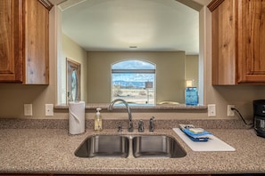 A kitchen with a double sink, granite countertop, wooden cabinets, a window with a view, and a coffee maker. - Hansel: Space, BLM Backdrop & BBQ Vibes! (Grand Junction)