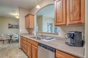 A modern kitchen with granite countertops, wooden cabinets, a dishwasher, and a coffee maker. - Hansel: Space, BLM Backdrop & BBQ Vibes! (Grand Junction)