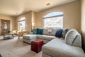 A living room with a sectional sofa, a red ottoman, and a large window offering a view of the sky. - Hansel & Gretel: Private 11-Acre Escape (Grand Junction)