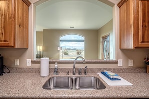 A kitchen with granite countertops, a double sink, wooden cabinets, and a window with a view of the outdoors. - Hansel & Gretel: Private 11-Acre Escape (Grand Junction)