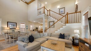 Un salon spacieux avec un grand canapé d’angle, une table basse en bois et un escalier menant à l’étage supérieur.