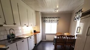 A kitchen with white cabinets, a stove, and a dining area with a table and chairs. - Västervik rum och stugor (Vastervik)