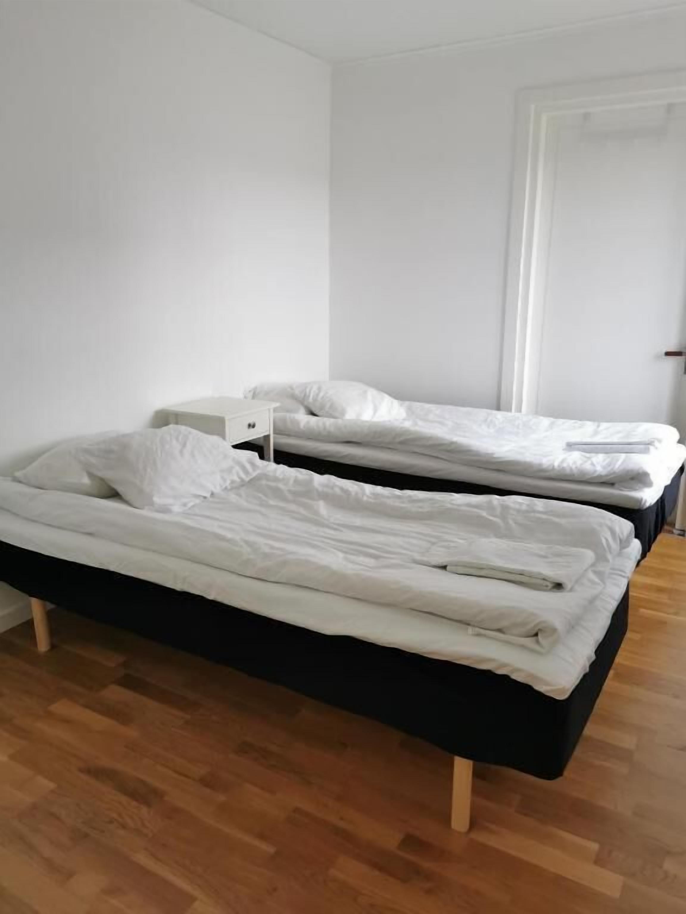 Une chambre avec deux lits simples, une petite table de chevet et une porte.