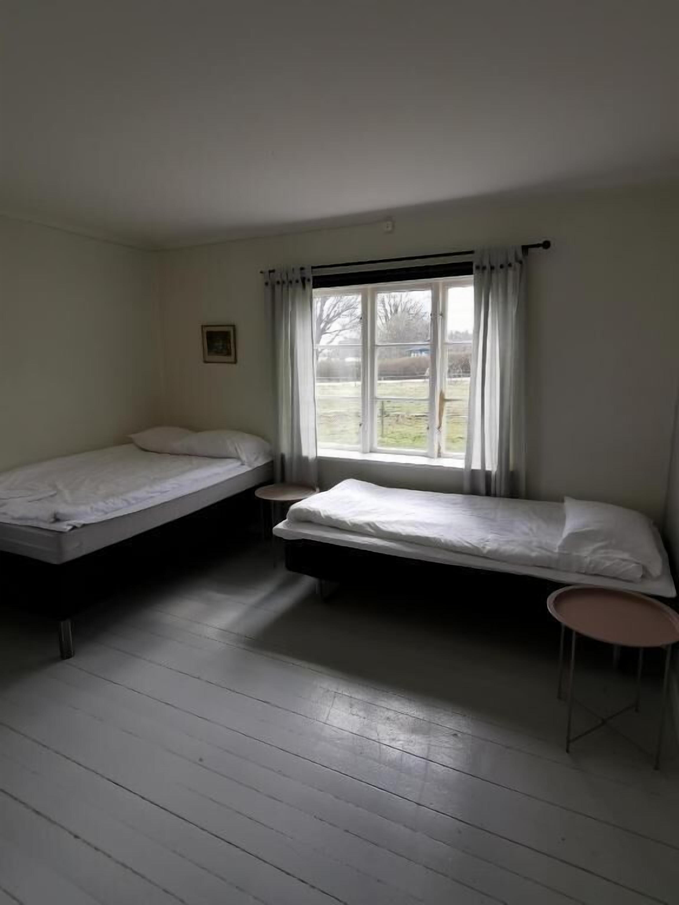 Una habitación con dos camas individuales, una mesita y una ventana con cortinas.