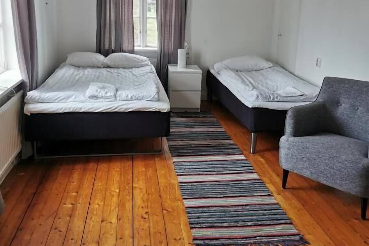 Ein Schlafzimmer mit zwei Betten, einem Nachttisch, einem Sessel und einem Streifen Teppich.