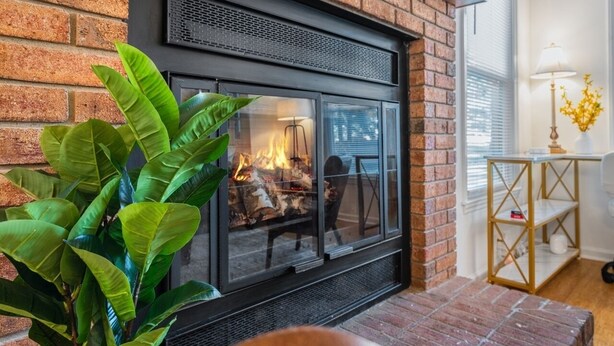 Una chimenea de ladrillo con puerta de vidrio, una planta en maceta y una lámpara sobre una mesita.