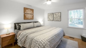 Un dormitorio con cama, mesita de noche, ventilador de techo y obras de arte en las paredes.