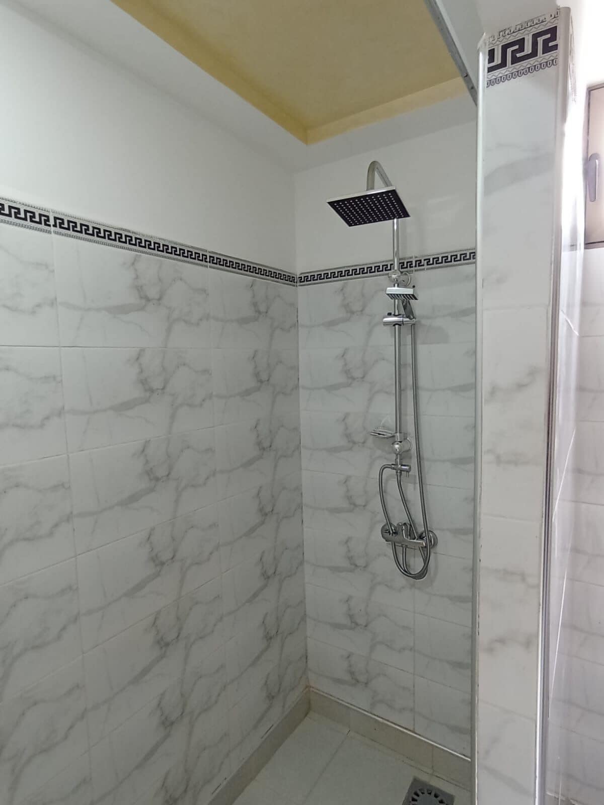 Une douche dotée d’un pommeau de douche à effet pluie et d’un pommeau de douche à main, de murs aux motifs de marbre et d’un plafond jaune.