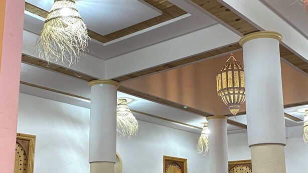 A room with a high ceiling, wooden beams, and white walls. There are columns supporting the ceiling, and a chandelier hanging from it. - Riad dreams dades  (Ait Sedrate Jbel El Soufla)