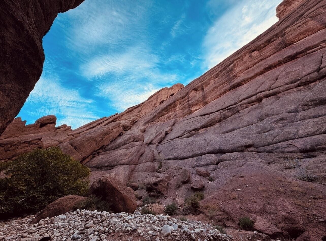 A rocky canyon with layered red rock formations and sparse vegetation.
