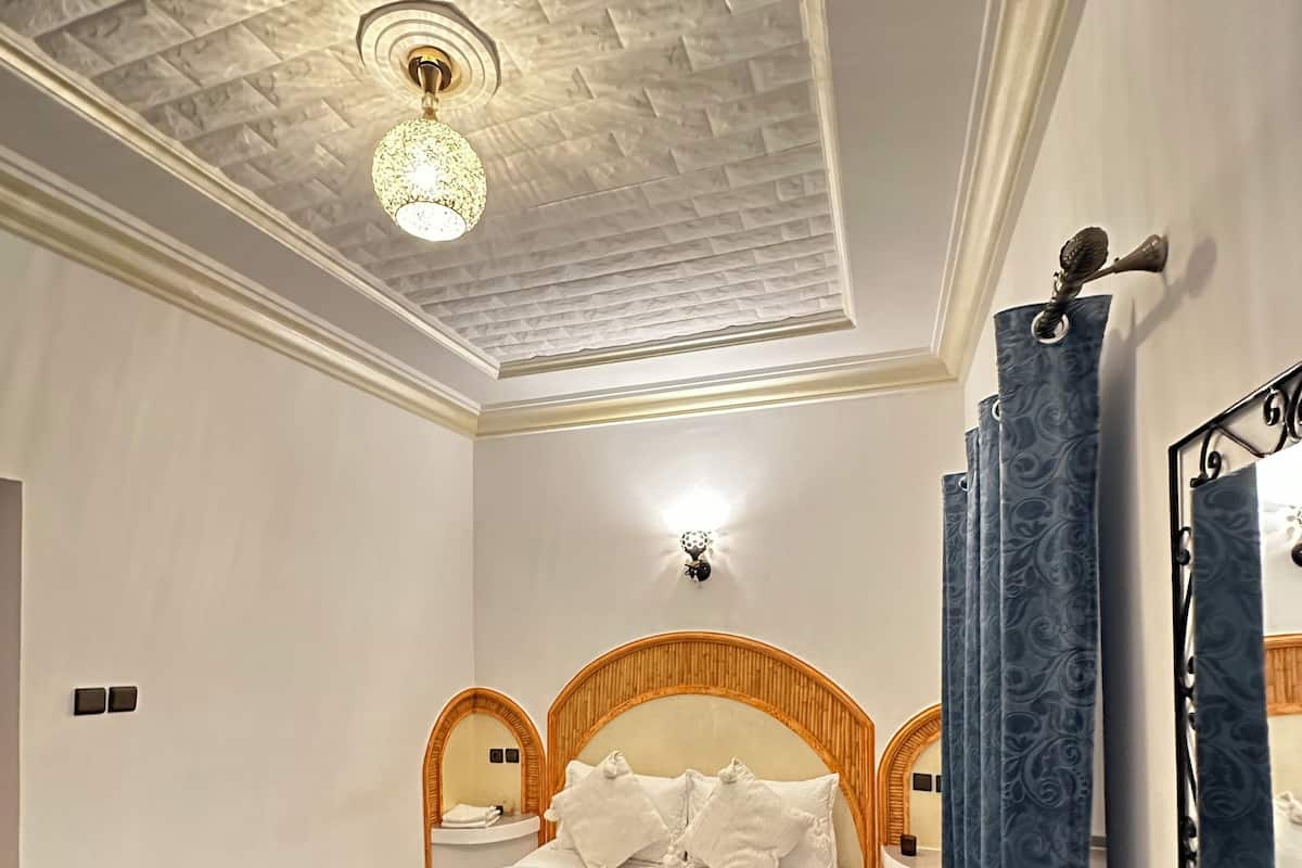 Un dormitorio con cama, mesita de noche, lámpara de pared y espejo.