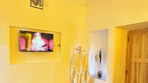 A room with a television mounted on the wall, a wooden table, a bathrobe, and a wooden door. - Riad dreams dades  (Ait Sedrate Jbel El Soufla)