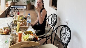 A person seated at a table with a variety of food items, including rice, vegetables, and bread. There are potted plants and a framed picture on the wall. - Riad dreams dades  (Ait Sedrate Jbel El Soufla)