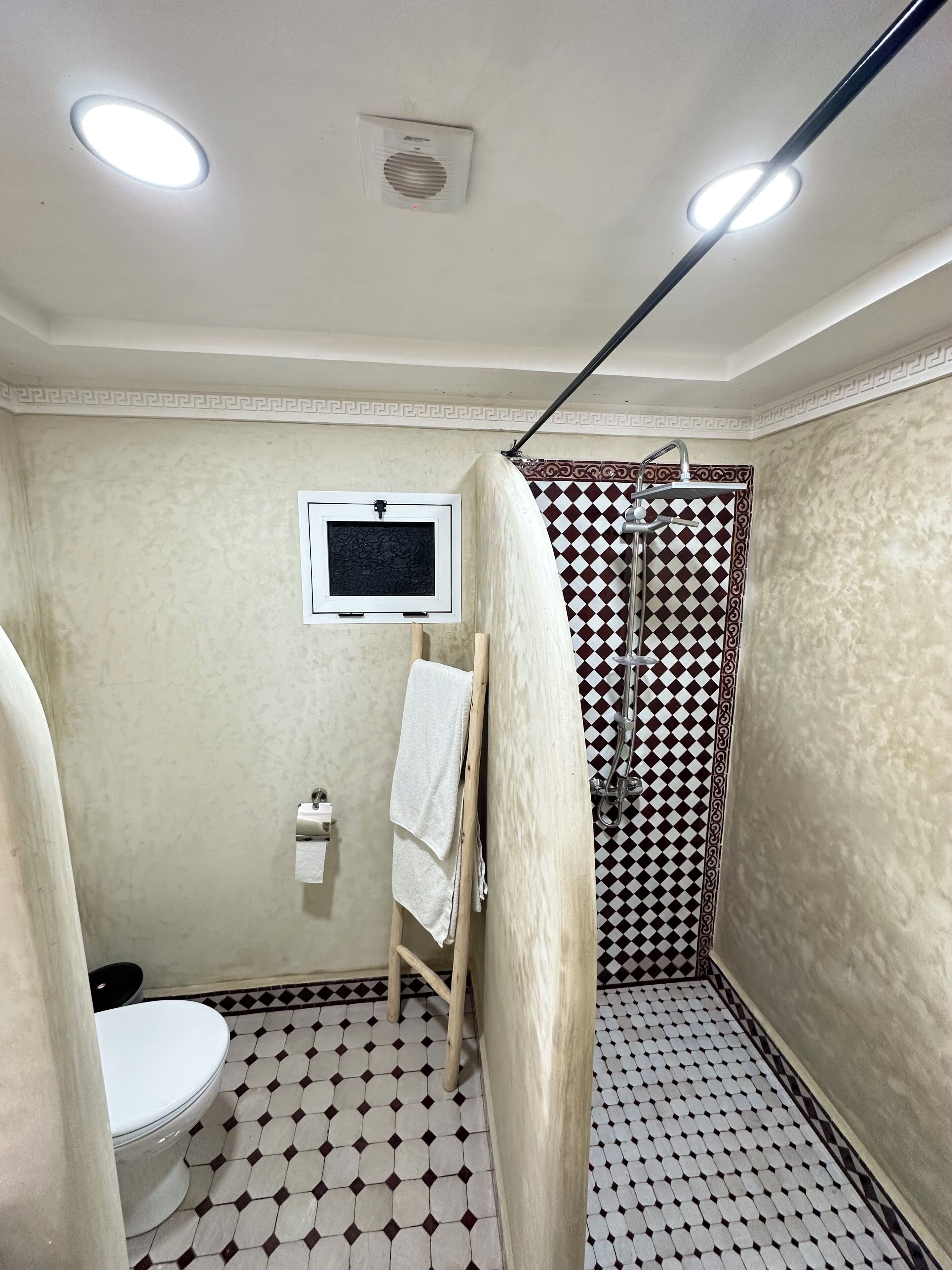 A bathroom with a toilet, a shower with a checkered pattern, and a towel rack.