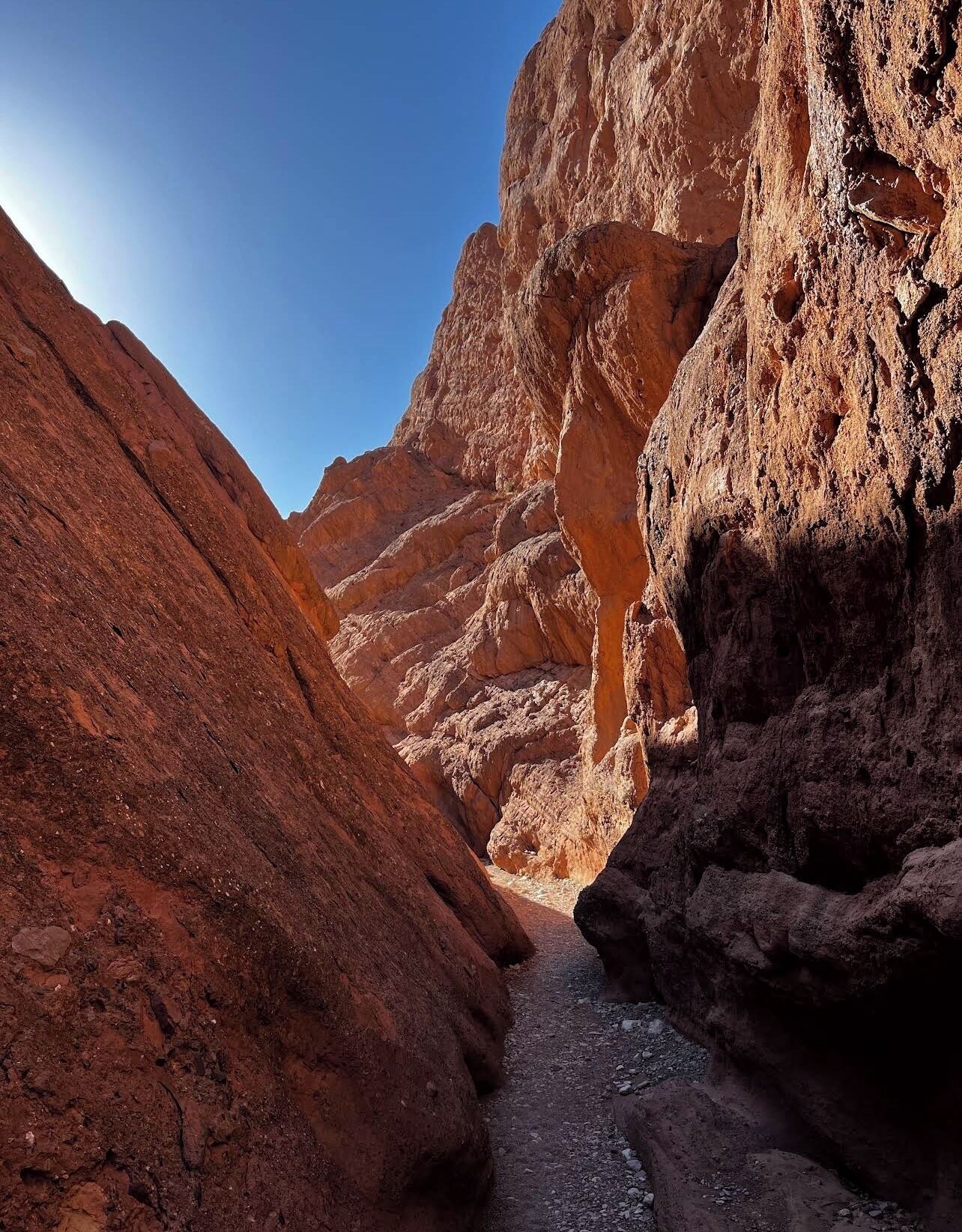 A narrow canyon with steep rock walls and a small stream running through it.