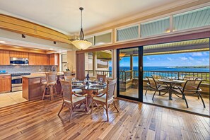 Een ruime keuken met houten kastjes en een groot eiland, een eetgedeelte met een glazen tafel, en een balkon met uitzicht op de oceaan.