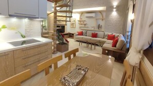 A modern kitchen with a central island, a dining area with a wooden table, and a living room with a sofa and a staircase.
