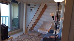 A living room with a sofa, a patterned rug, a chair, a TV, a lamp, and a staircase. - Appartement vue sur mer (Soulac sur Mer)