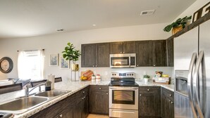 A modern kitchen with dark wood cabinets, stainless steel appliances, a granite countertop, and a window with curtains. - Colorado Springs Family Home ~ 10 Mi to Downtown! (Colorado Springs)