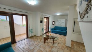 A living room with a glass coffee table, a blue sofa, and a sliding glass door leading to a balcony. - 3 Bedroom Villa in Pittulongu (Pittulongu)