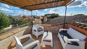 An outdoor patio with white wicker furniture, a table with a glass, and a view of the surrounding area. - 3 Bedroom Villa in Pittulongu (Pittulongu)