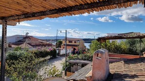 A view from a covered outdoor area overlooking a town with traditional architecture, a body of water, and mountains in the distance. - 3 Bedroom Villa in Pittulongu (Pittulongu)