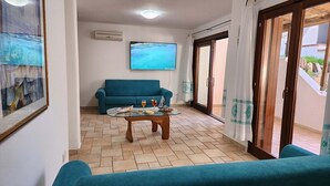 A living room with a blue sofa, a coffee table with drinks, and a TV on the wall. - 3 Bedroom Villa in Pittulongu (Pittulongu)