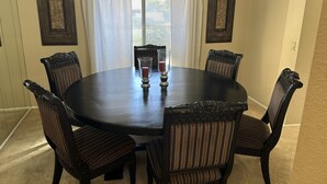 A dining room with a round table, six upholstered chairs, and two candle holders.