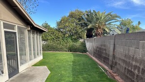 A well-maintained backyard with a lawn, a concrete patio, and a stone wall.
