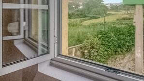 Ein Fenster mit Blick auf eine grüne Landschaft, darunter Gras, Büsche und ein Zaun.