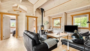 A cozy log cabin interior with a fireplace, leather sofas, a flat-screen TV, and large windows offering a view of greenery. - Beautiful home in Hemmet with kitchen (Hemmet)