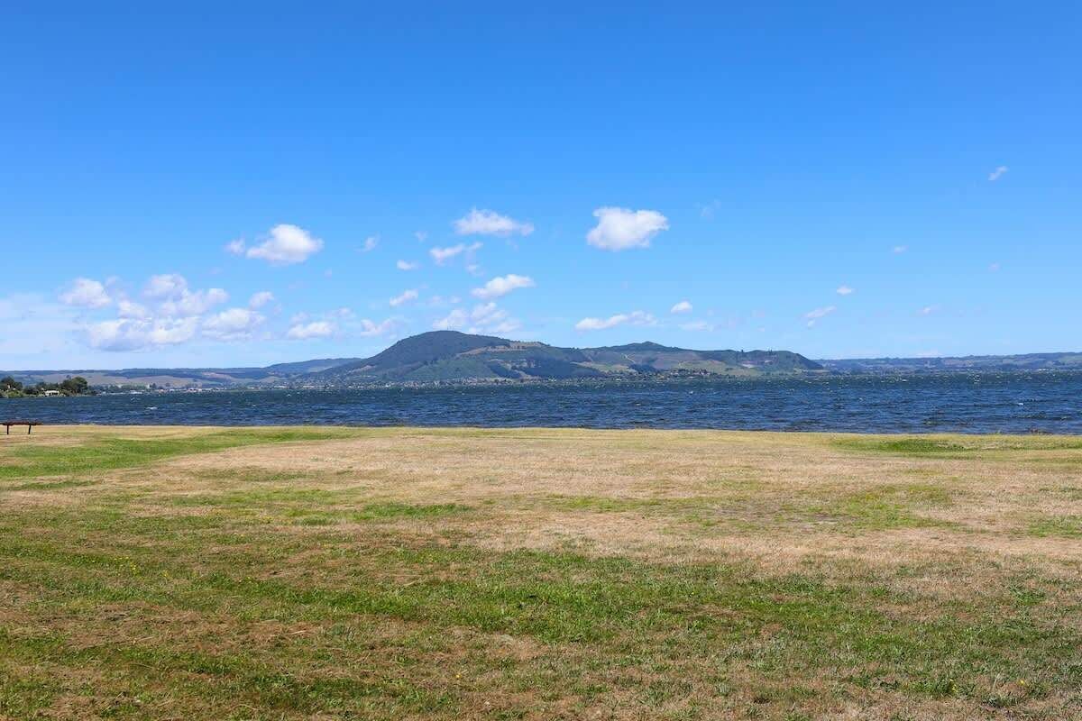 A grassy field with a body of water and distant mountains under a clear sky.