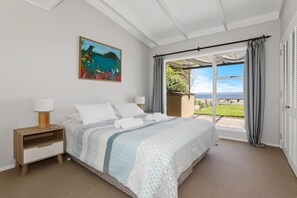 A bedroom with a bed, a nightstand, a painting, and a view of the outdoors.