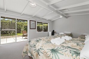A bedroom with a large bed, a desk, and a chair. There are windows providing a view of the outdoors. - Hannah's Bay Lakefront - Kayaks, Sleeps 8 (Rotorua)