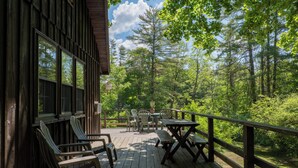 Une terrasse en bois avec des fauteuils Adirondack et une table de pique-nique, donnant sur une zone boisée.