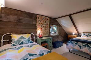 Un dormitorio acogedor en el ático con paredes de madera, techo inclinado y dos camas con colchas estampadas.