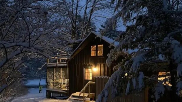 Une cabane en bois dotée d’un porche vitré, entourée d’arbres couverts de neige.
