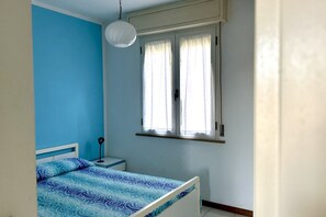 Ein Schlafzimmer mit einem Bett, einem Nachttisch, einer Lampe und einem Fenster mit Vorhängen.