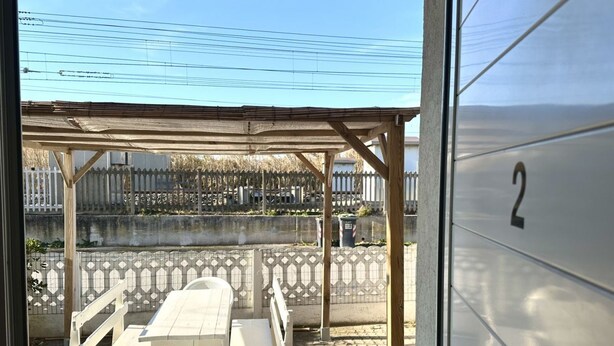 A covered outdoor seating area with a table and chairs, a fence, and a building with the number '2' on it. - F002 - Fano, three-room apartment with porch 30m from the sea (Fano)