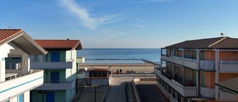 A coastal building with multiple balconies, a beach in the background, and a clear sky.