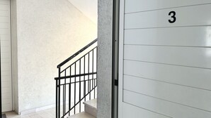 Ein Korridor mit weißer Wand, schwarzer Geländer und einer Tür mit der Nummer 3.