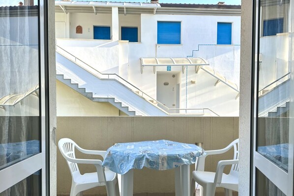 A balcony with a table and chairs, a staircase, and a building with blue shutters.