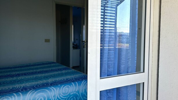 Una habitación con cama, puerta y ventana con cortinas.