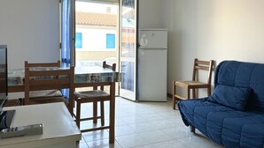 Un espacio habitable compacto con una mesa de comedor, sillas, un sofá, un refrigerador y un ventanal corredero que da a un área exterior.