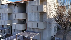Un edificio de varios pisos con balcones, un espacio de estar al aire libre cubierto y un árbol en primer plano.