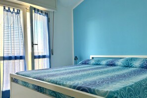 Een slaapkamer met een bed, gordijnen en een effen gekleurde muur.