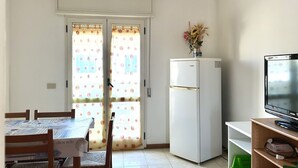 Une petite cuisine équipée d’un réfrigérateur, d’une table à manger avec des chaises et d’un téléviseur posé sur un meuble.