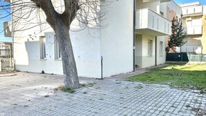 Un bâtiment avec un arbre devant, un trottoir pavé et une zone herbeuse.