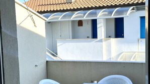 Un balcon avec une table et des chaises, une porte bleue et un mur blanc.