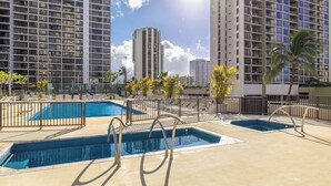 A rooftop pool area with multiple swimming pools, surrounded by tall buildings and palm trees. - Ocean View Waikiki Condo with Free Parking -- Short Walk to Beach (Honolulu)